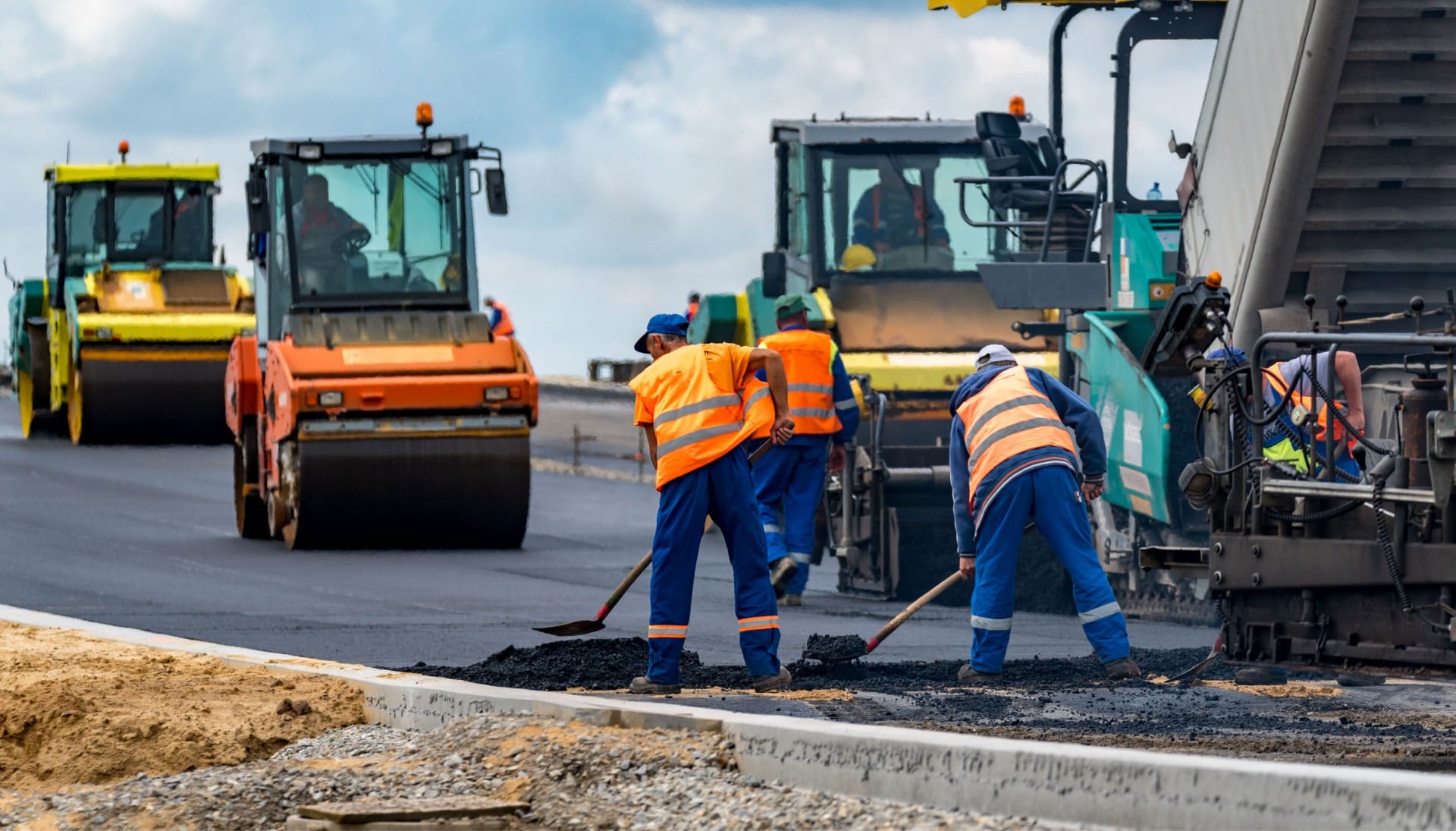 A group of construction workers wearing hard hats and reflective vests, operating heavy machinery and laying down asphalt on a newly excavated road in Durham, showcasing the intricate process of building a sturdy and smooth surface.